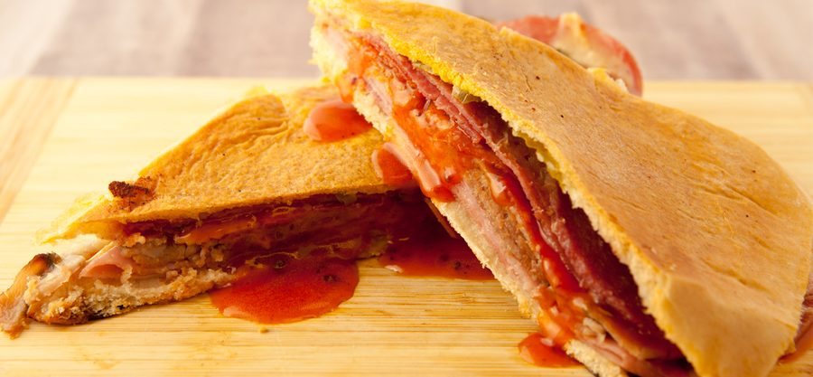 A Tropi Shack Cuban sandwich cut in half on a wooden board